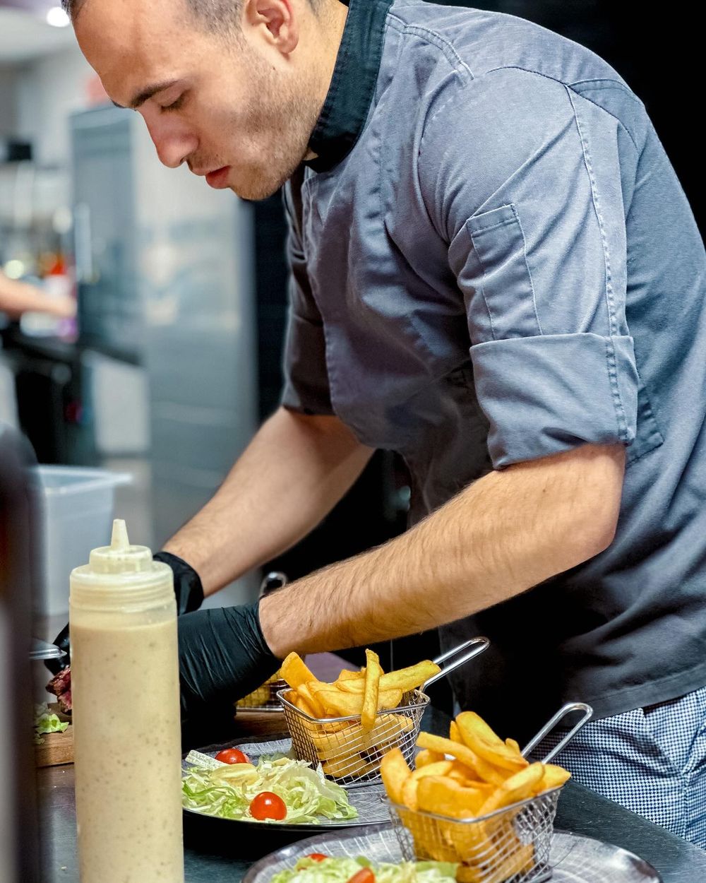 Le cuisinier dresse des assiettes de frites et de salade dans la cuisine du restaurant