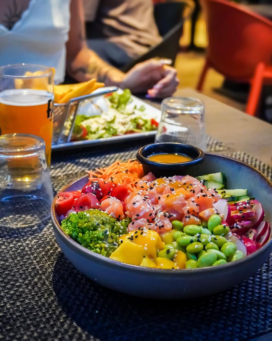 Un bol coloré garni de poisson cru, edamame, mangue, concombre et carotte, avec une bière à côté